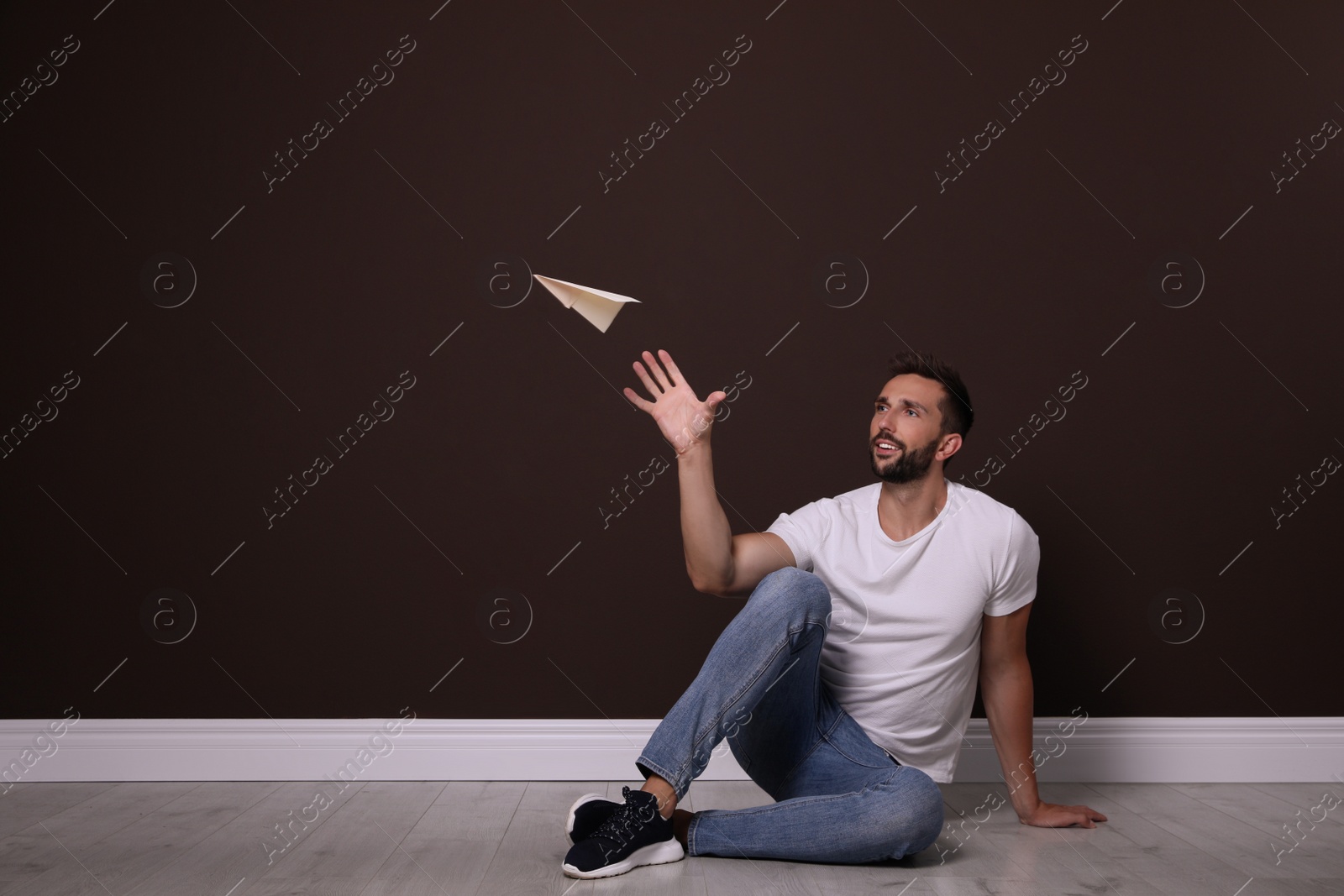 Photo of Handsome man playing with paper plane near brown wall. Space for text
