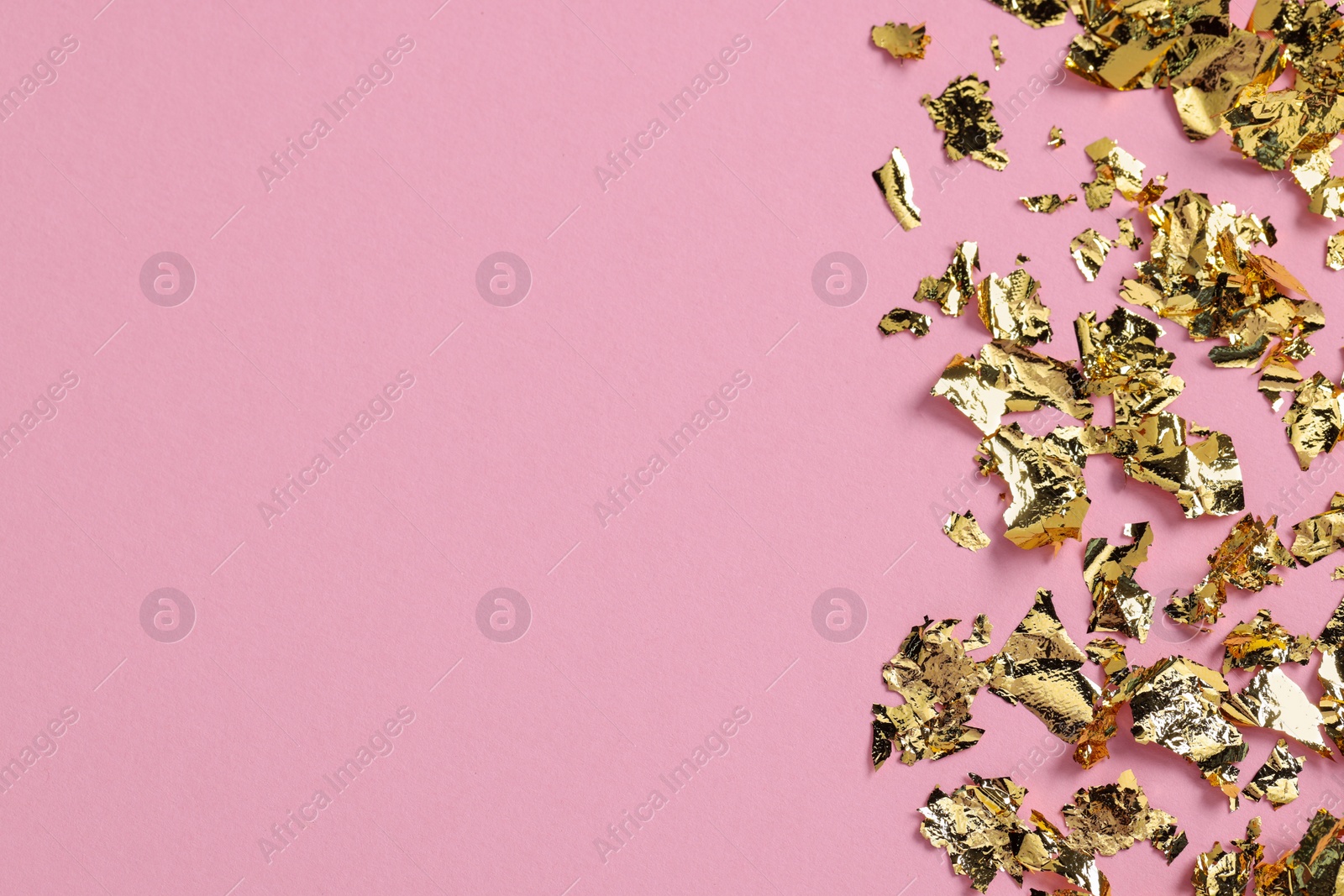 Photo of Many pieces of edible gold leaf on pink background, flat lay. Space for text