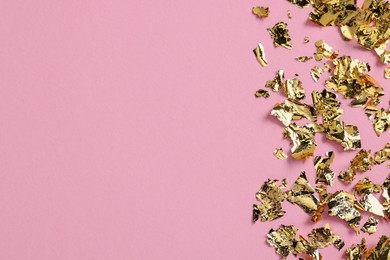 Photo of Many pieces of edible gold leaf on pink background, flat lay. Space for text