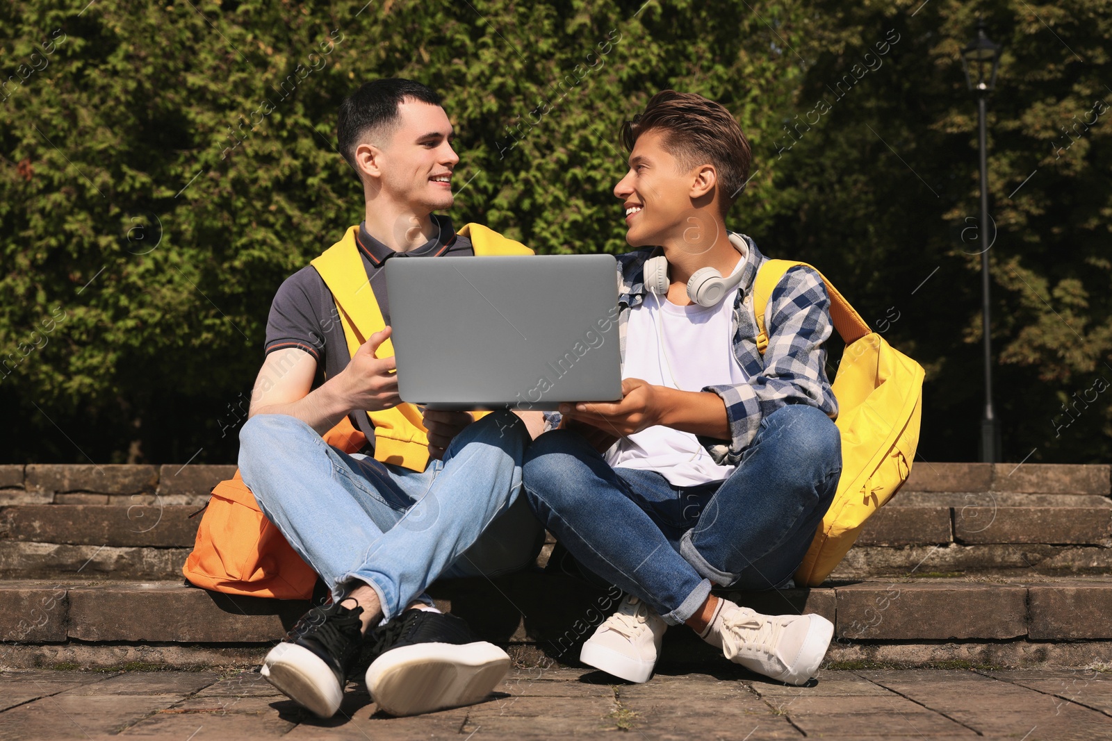 Photo of Happy young students studying with laptop together on steps in park