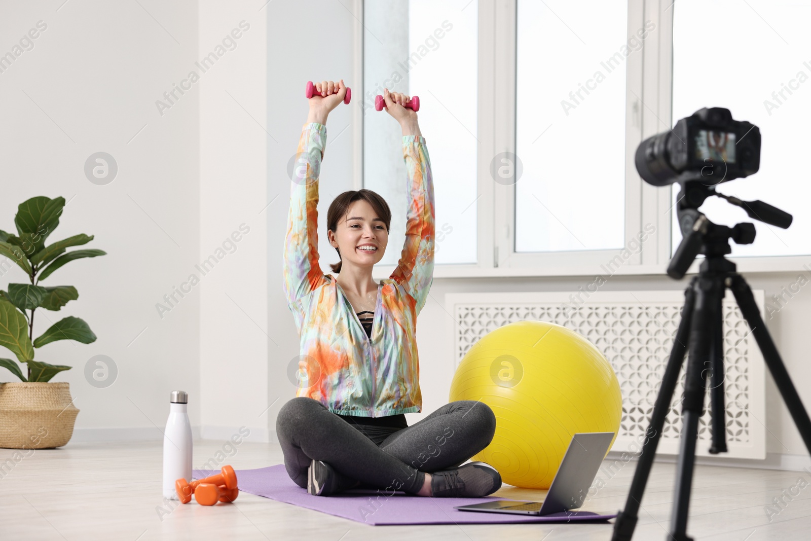 Photo of Happy sports blogger training with dumbbells while recording fitness lesson at home