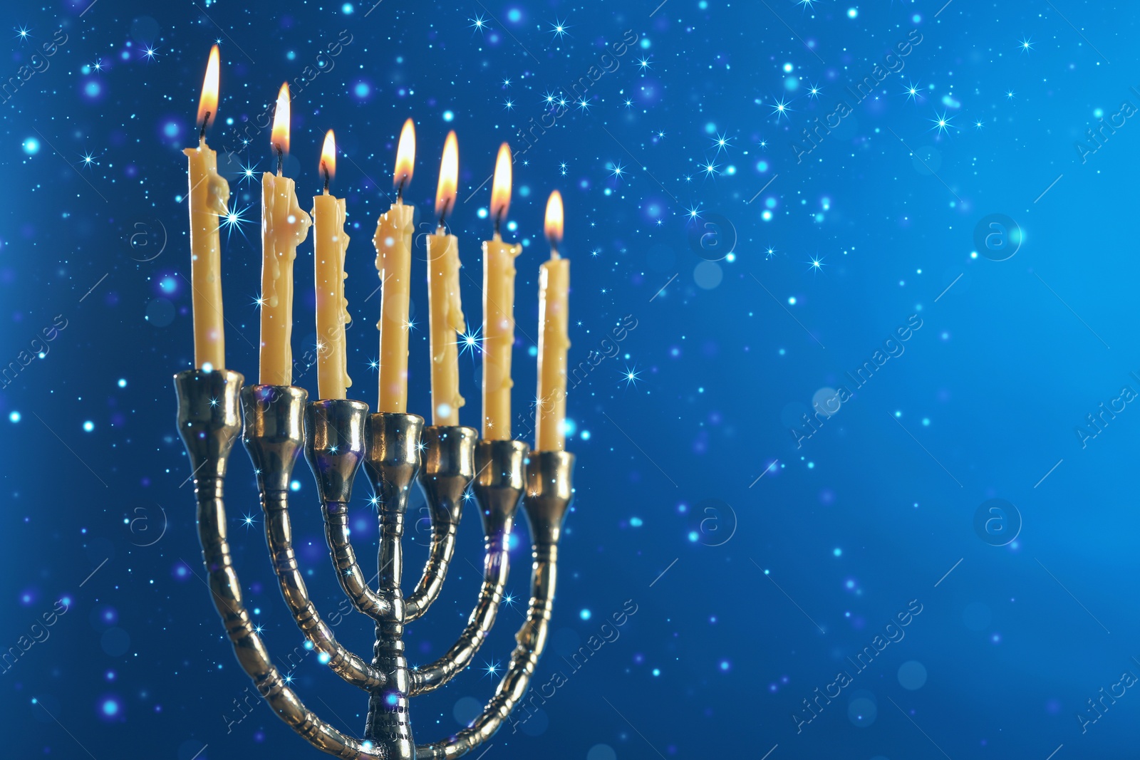 Image of Hanukkah celebration. Menorah with burning candles on blue background, space for text