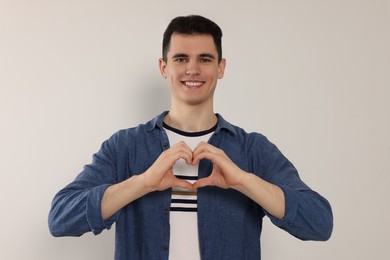 Photo of Happy volunteer making heart with his hands on light background