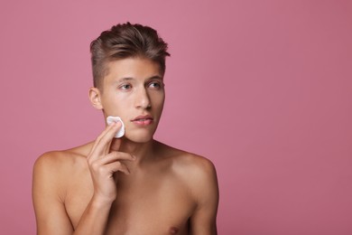 Handsome man cleaning face with cotton pad on pink background, space for text