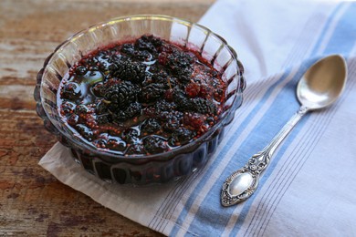 Bowl of sweet black mulberry jam, napkin and spoon on wooden table