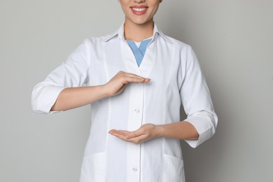 Photo of Young doctor holding something on light grey background, closeup