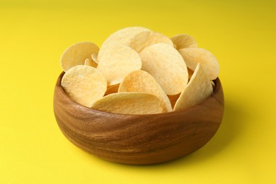 Bowl of tasty potato chips on yellow background