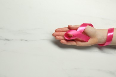 Photo of Breast cancer awareness. Woman with pink ribbon at white marble table, top view. Space for text