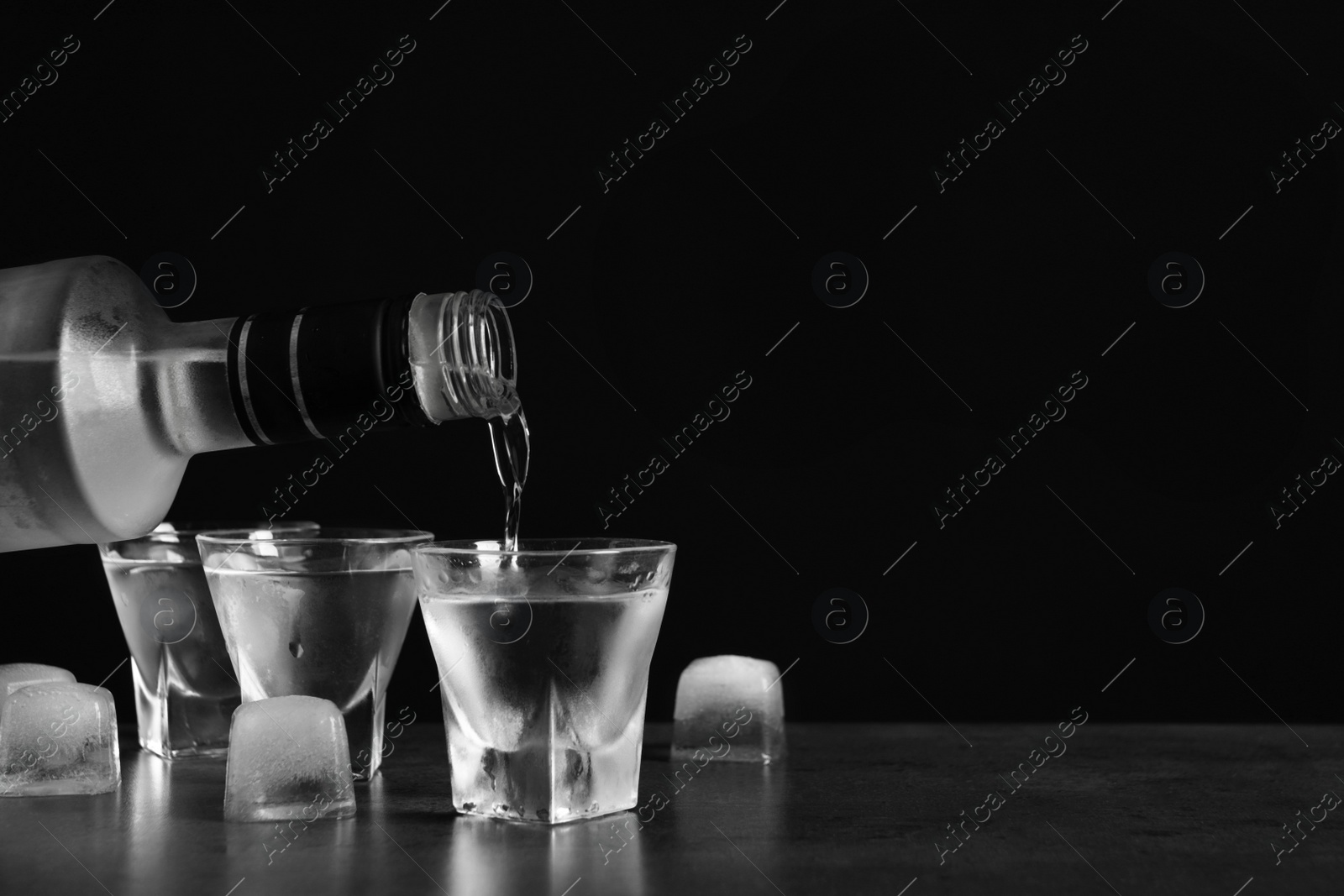 Photo of Pouring vodka from bottle in glass and ice cubes on grey table. Space for text