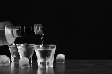 Photo of Pouring vodka from bottle in glass and ice cubes on grey table. Space for text