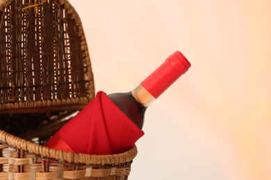 Photo of Wicker basket with bottle of wine against blurred background, closeup. Space for text