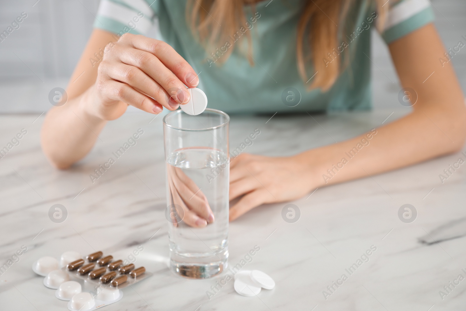 Photo of Woman putting medicine for hangover into glass of water indoors, closeup