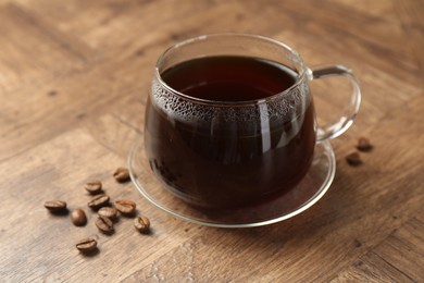 Photo of Hot coffee in glass cup and beans on wooden table, closeup