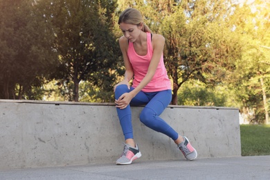 Photo of Young woman in sportswear having knee problems in park