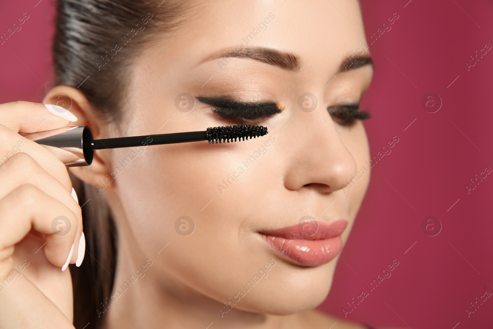Photo of Beautiful woman applying mascara on pink background, closeup. Stylish makeup