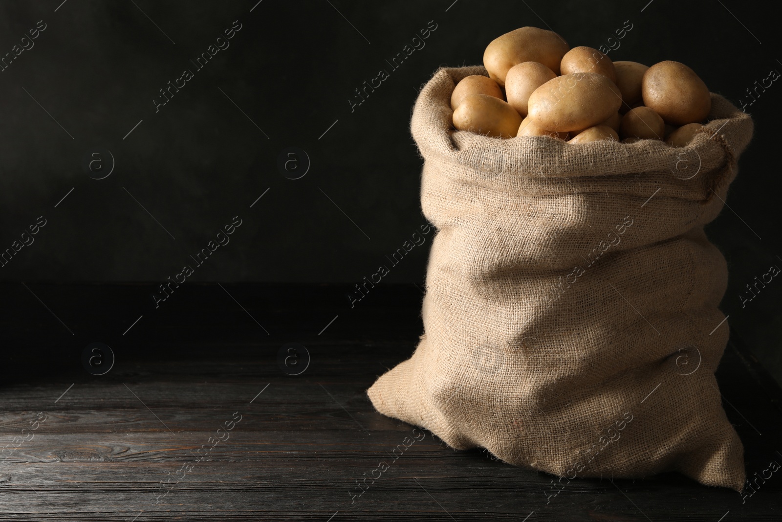 Photo of Raw fresh organic potatoes on wooden table against dark background. Space for text