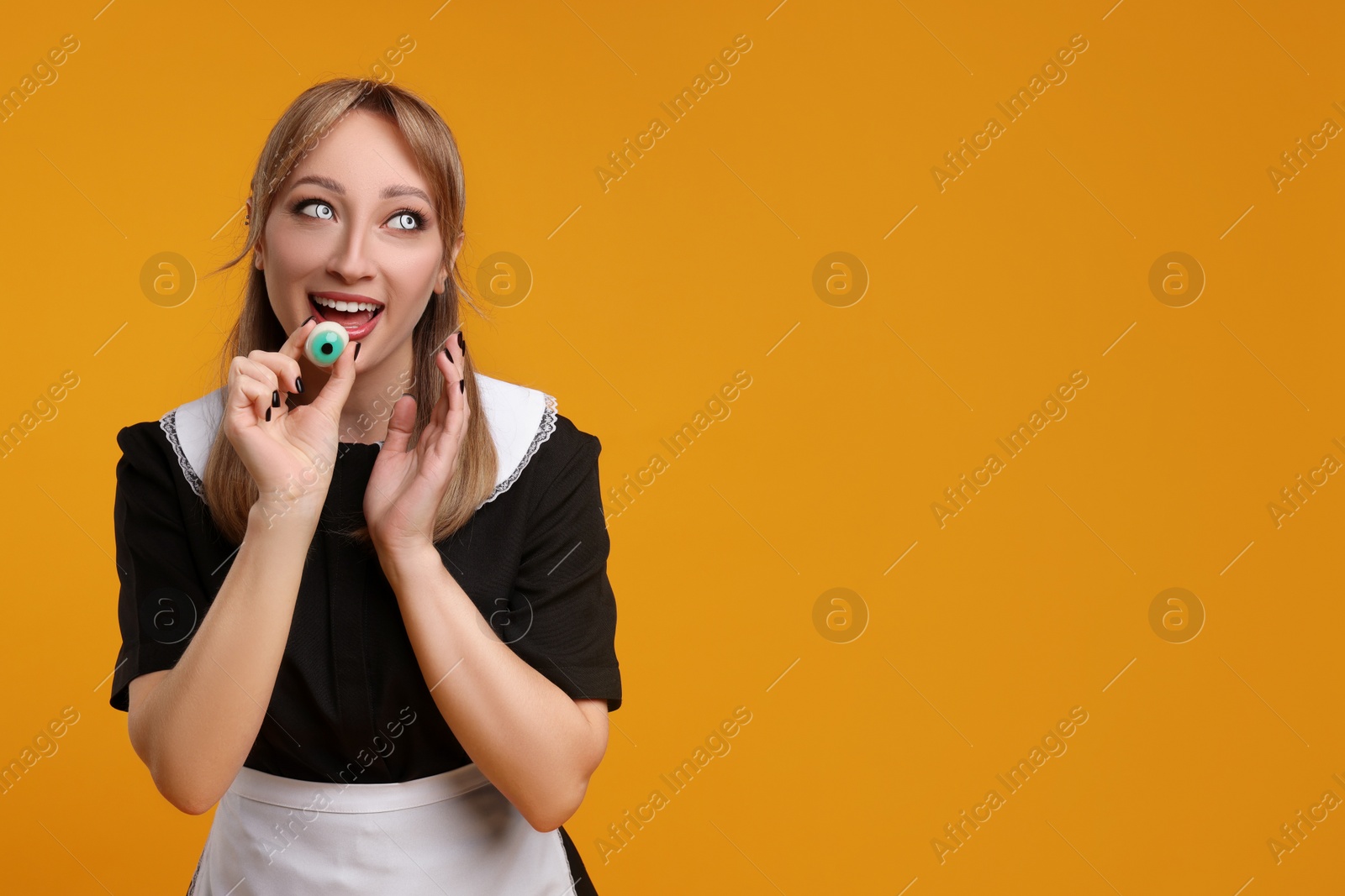 Photo of Happy woman in scary maid costume with decorative eyeball on orange background, space for text. Halloween celebration