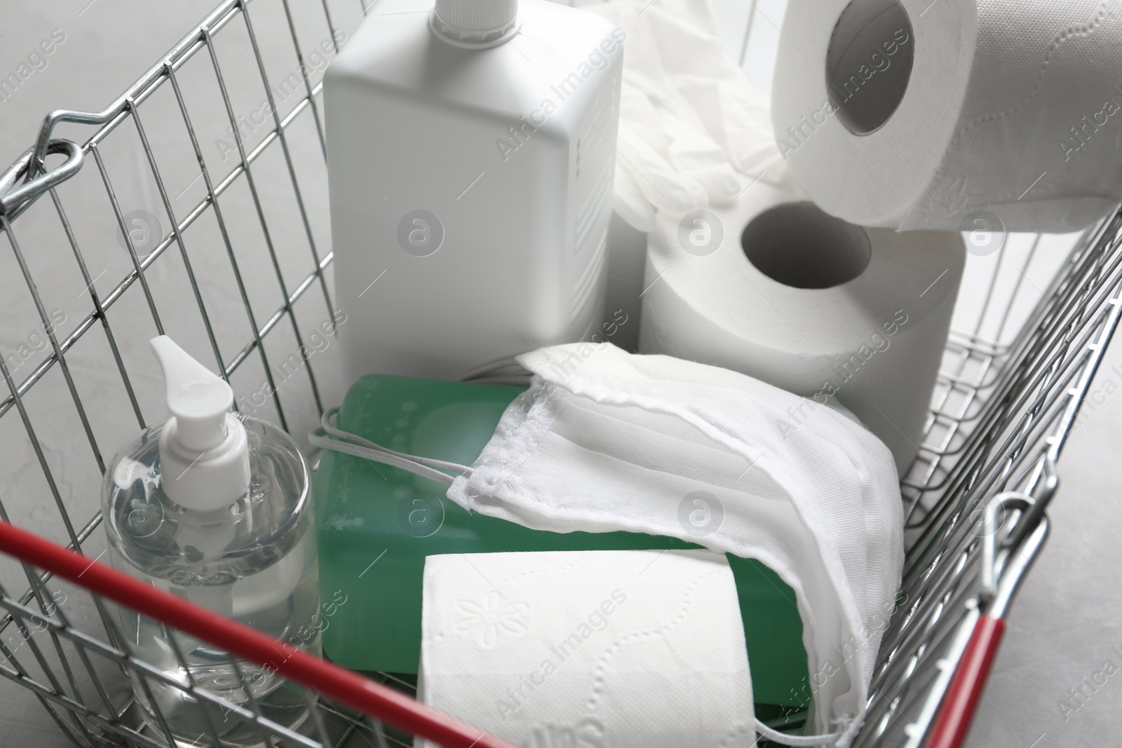 Photo of Shopping basket with antiseptics, toilet paper, gloves and masks on grey table, closeup. Panic caused by virus