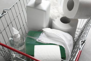 Photo of Shopping basket with antiseptics, toilet paper, gloves and masks on grey table, closeup. Panic caused by virus