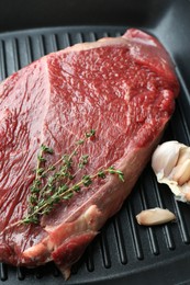 Grill pan with piece of raw beef meat, garlic and thyme, closeup