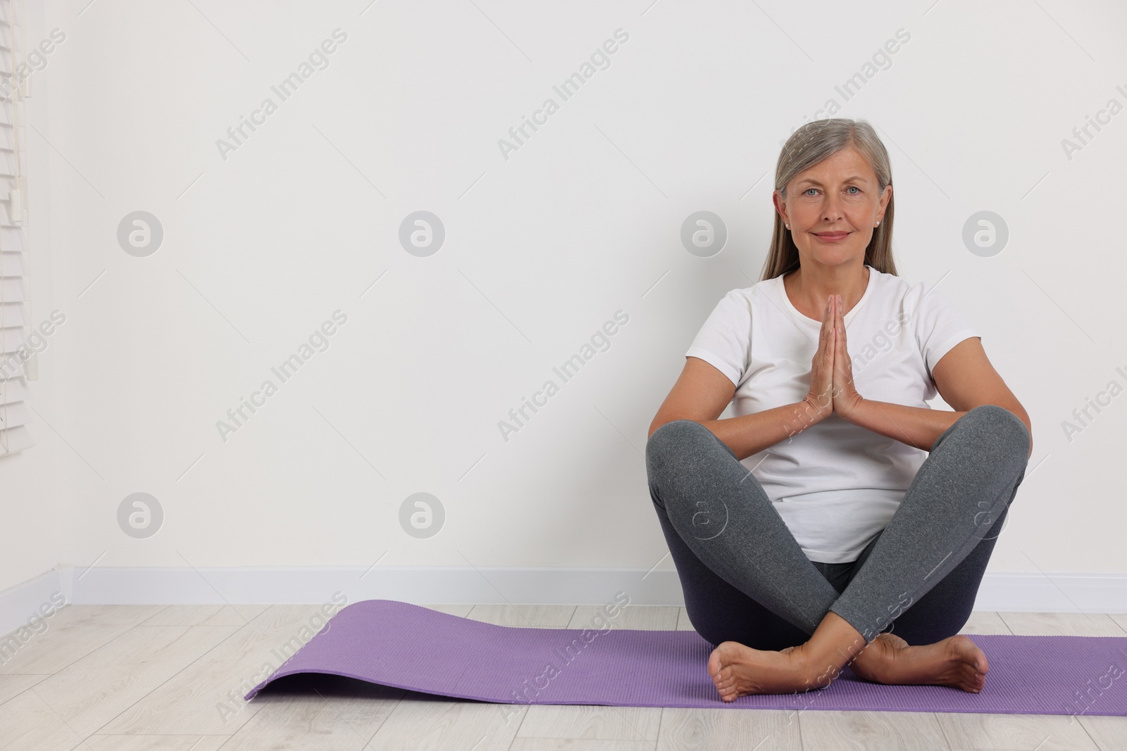 Photo of Happy senior woman practicing yoga on mat near white wall. Space for text