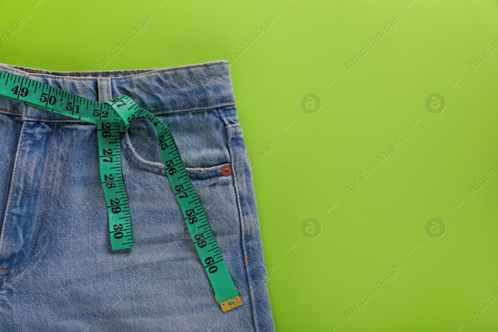 Photo of Jeans and measuring tape on light green background, top view with space for text. Weight loss concept