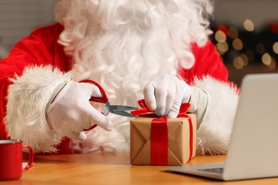 Photo of Santa Claus with scissors decorating Christmas gift at home, closeup