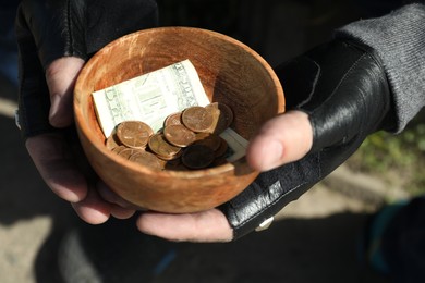 Poor homeless man holding bowl with donations on blurred background, closeup