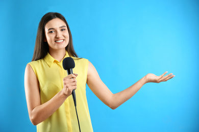 Photo of Young female journalist with microphone on blue background