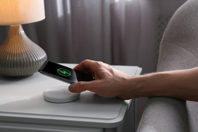 Photo of Man putting smartphone on wireless charger in room, closeup