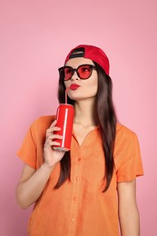 Photo of Beautiful young woman drinking from tin can on pink background