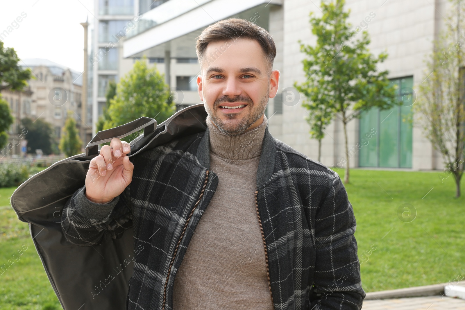 Photo of Man holding garment cover with clothes outdoors. Dry-cleaning service