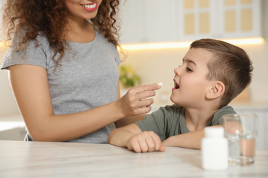 African-American woman giving vitamin pill to little boy in kitchen