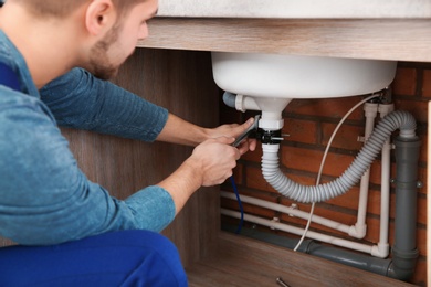 Male plumber in uniform repairing kitchen sink