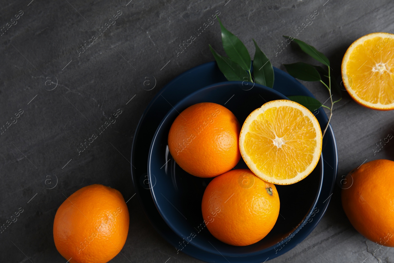 Photo of Fresh oranges and bowl on grey table, top view with space for text