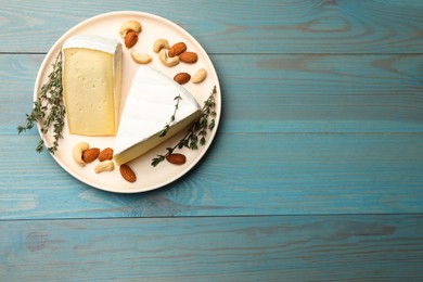 Photo of Tasty Camembert cheese with thyme and nuts on light blue wooden table, top view. Space for text