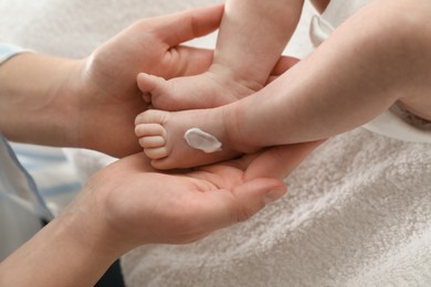 Photo of Mother applying body cream on her little baby indoors, closeup