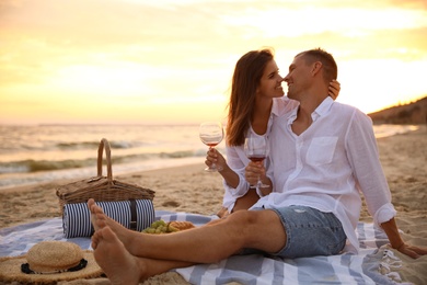 Photo of Lovely couple having romantic picnic on beach at sunset