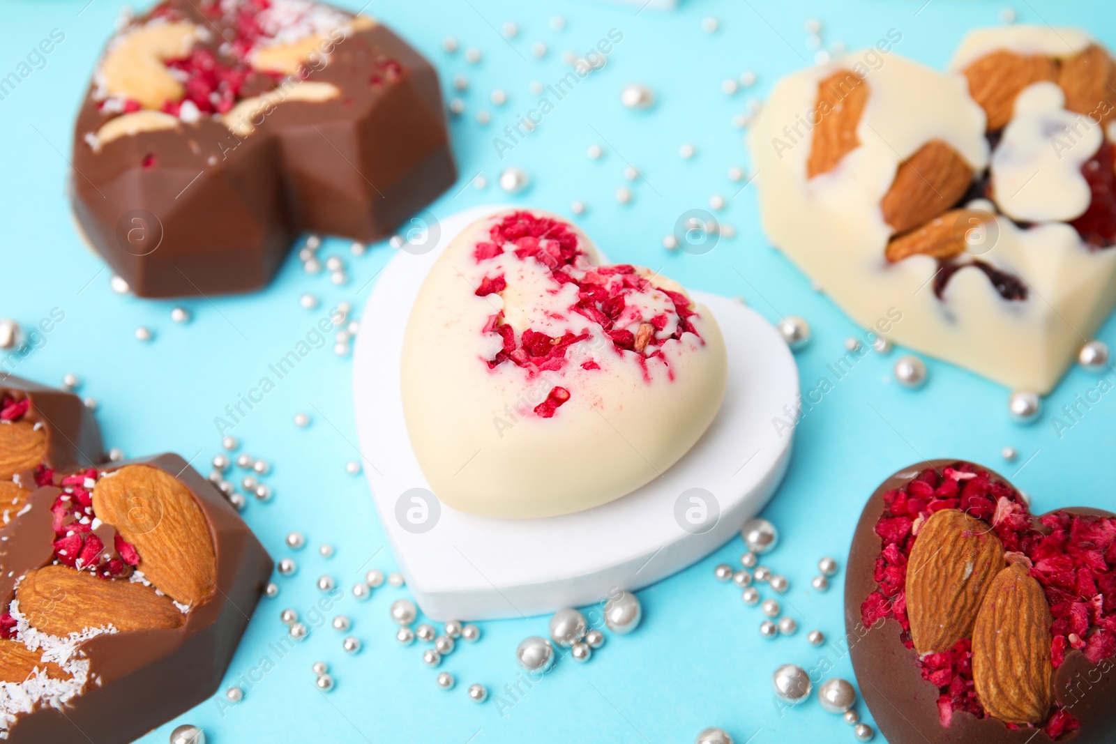 Photo of Tasty chocolate heart shaped candies with nuts on light blue background