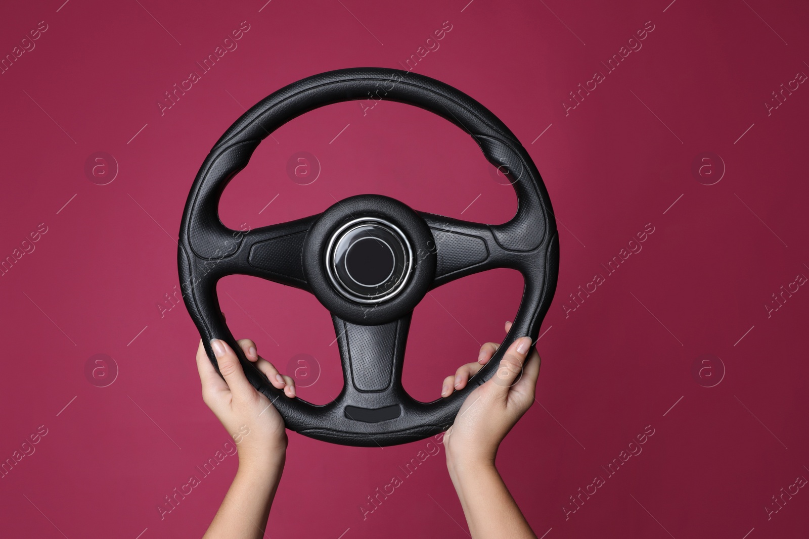 Photo of Woman holding steering wheel on crimson background, closeup