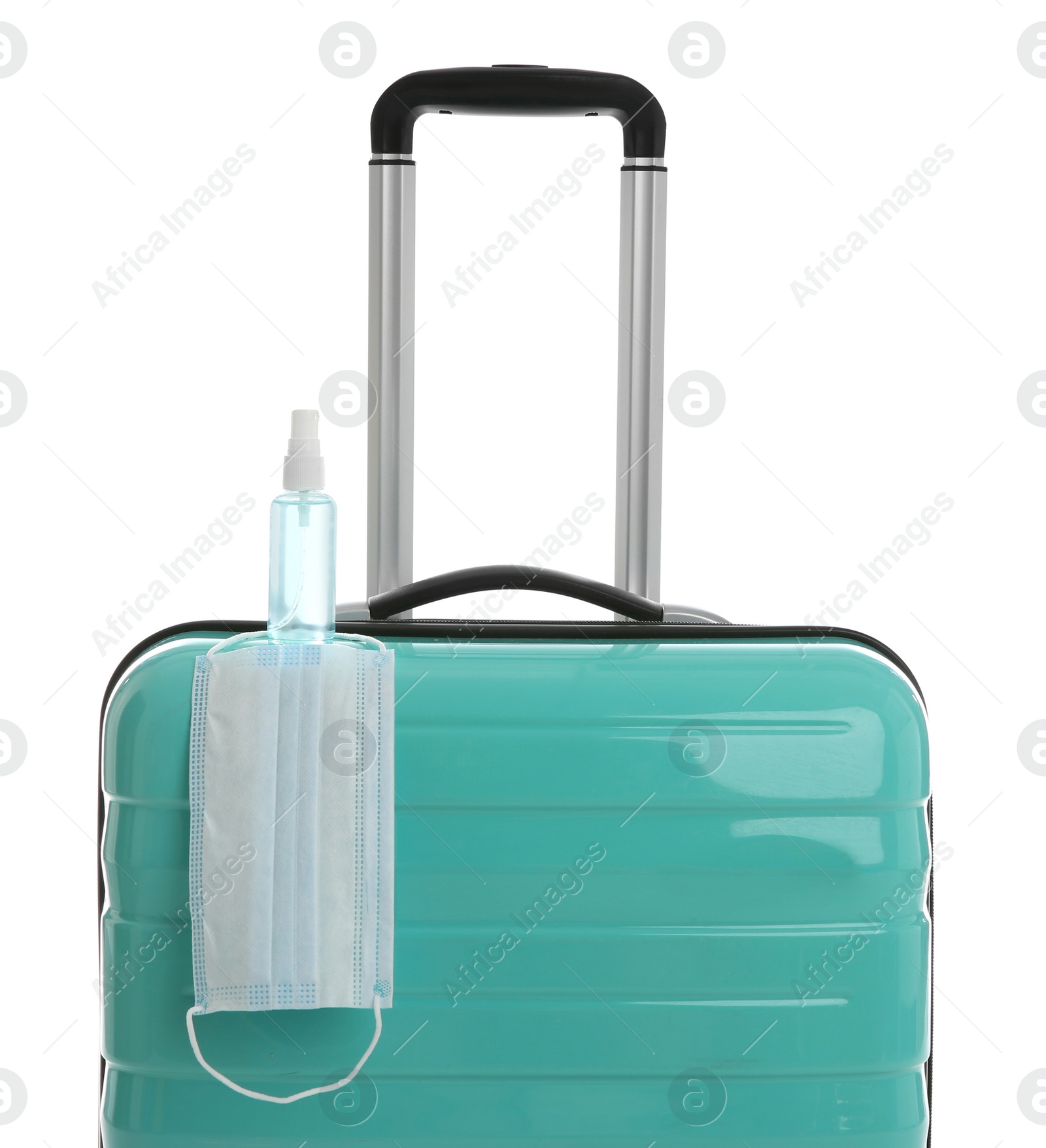 Photo of Stylish turquoise suitcase, antiseptic spray and protective mask on white background. Travelling during coronavirus pandemic