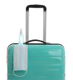 Stylish turquoise suitcase, antiseptic spray and protective mask on white background. Travelling during coronavirus pandemic