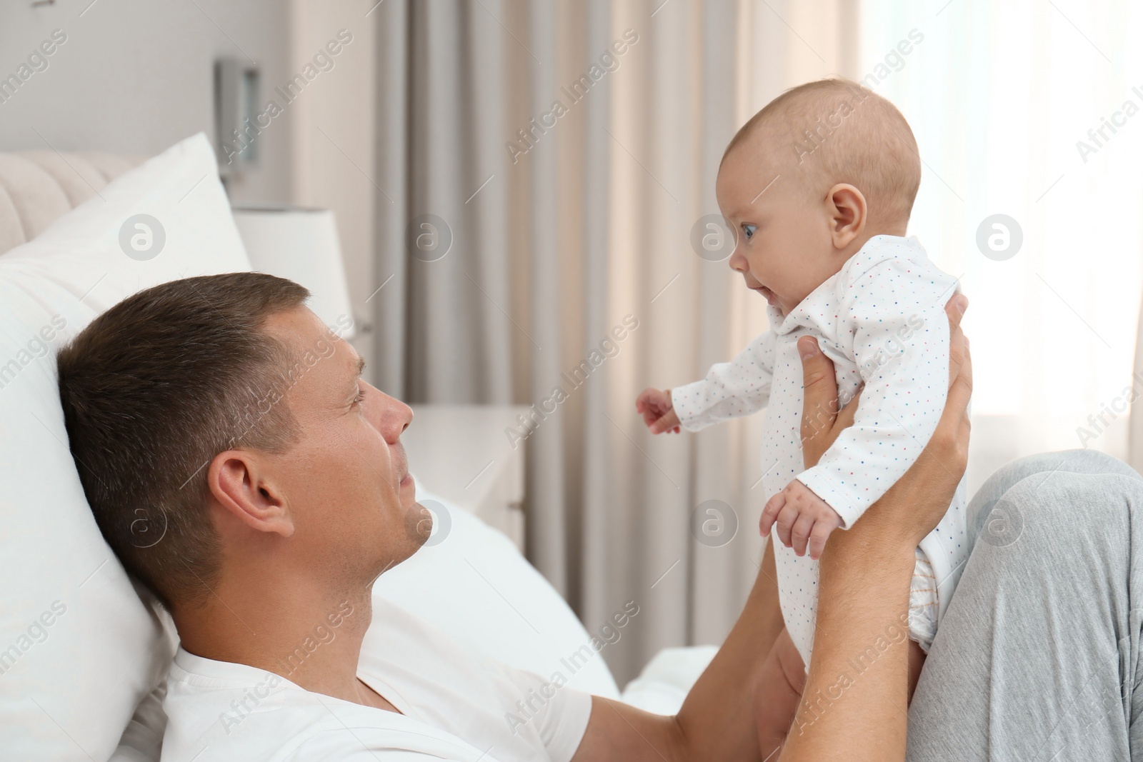 Photo of Happy father holding his cute baby on bed at home