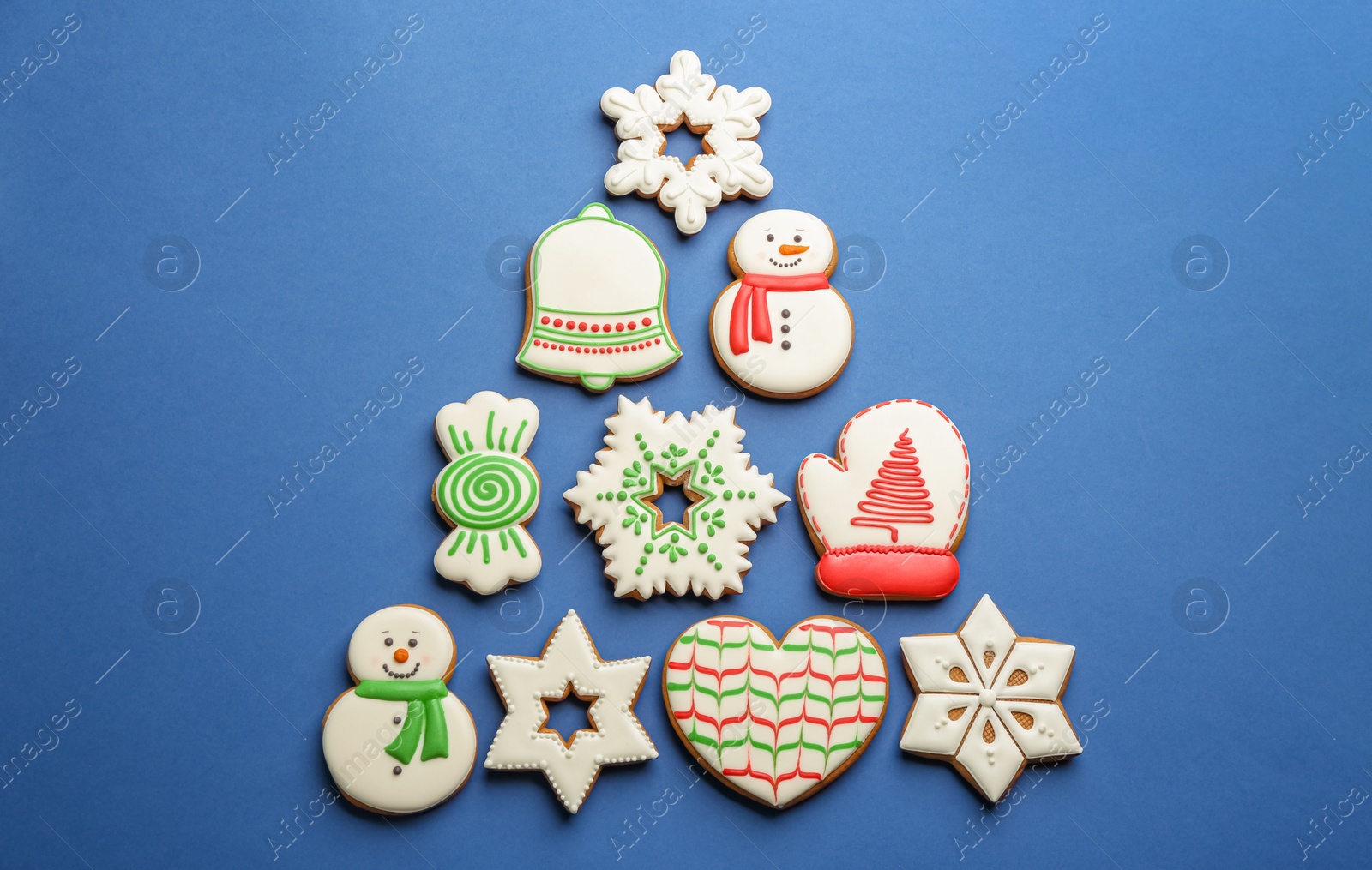 Photo of Christmas tree shape made of delicious decorated gingerbread cookies on blue background, flat lay