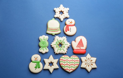 Photo of Christmas tree shape made of delicious decorated gingerbread cookies on blue background, flat lay