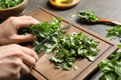 Photo of Woman cutting fresh green cilantro at grey table, closeup