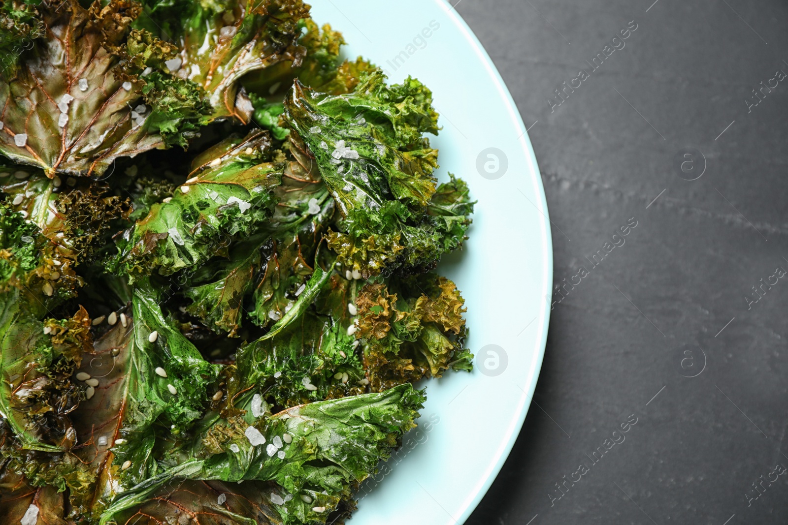 Photo of Tasty baked kale chips on dark grey table, top view