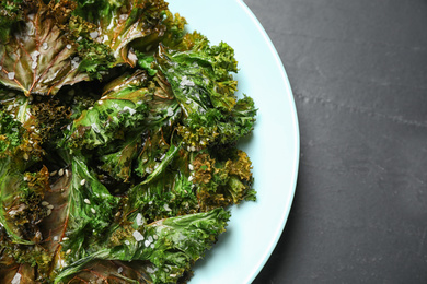 Tasty baked kale chips on dark grey table, top view