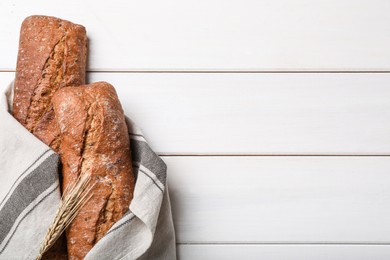 Photo of Tasty rye baguettes and spikelet on white wooden table, flat lay. Space for text