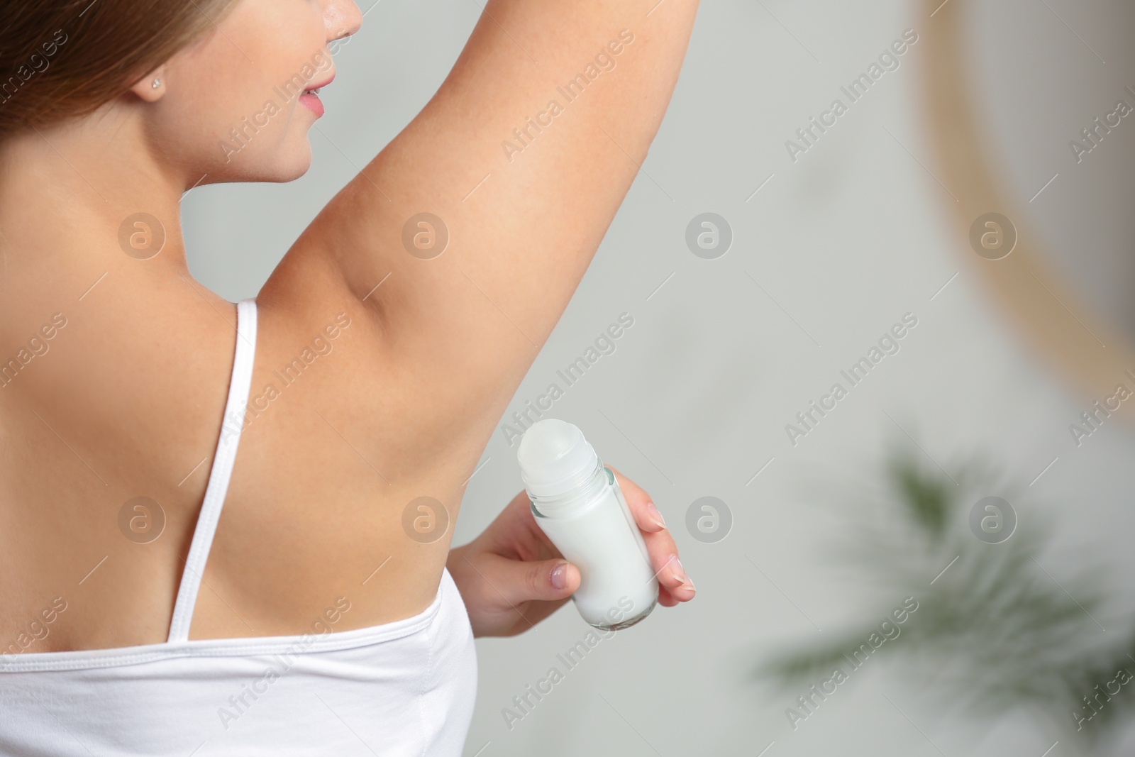 Photo of Young woman applying roll-on deodorant indoors, closeup. Space for text